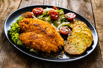 Breaded fried pork chop with fried potatoes and greens on wooden table
