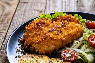Breaded fried pork chop with fried potatoes and greens on wooden table
