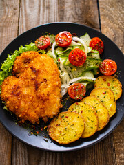 Breaded fried pork chop with fried potatoes and greens on wooden table

