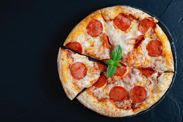 Hot pepperoni pizza and basil on black concrete background. Top view of hot pepperoni pizza. With copy space for text