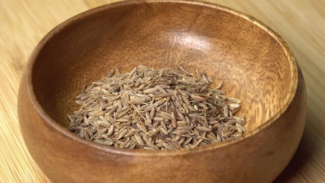 Dried cumin spice seeds lies in wooden bowl and rotating on wooden board. Dry seasoning in spoon. Spices and herbs for cooking zira