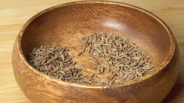 Spoon picks up dried cumin spice seeds from wooden bowl and rotating on wooden board. Dry seasoning in spoon. Spices and herbs for cooking zira
