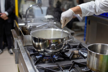 A cook stirring pots in the kitchen. Big pots in the kitchen