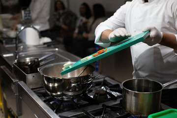 The cook pours the vegetables from the cutting board into the pot. The cook is cooking.