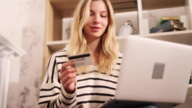 Soft dreamy portrait of young pretty blond woman paying with credit card on laptop computer in the light living room Happy customer doing payments online shopping in internet store easy pay at home