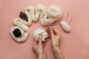 woman hand holding needle felting kit. felted woolen needle and skein of wool on pink table, flat lay