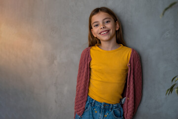 Beautiful young girl wearing mustard yellow blouse and a cardigan looking at camera and smiling. Human emotions and facial expressions concept.