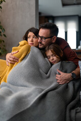 Father trying to warm his family up because they are feeling cold covered with a blanket at home.