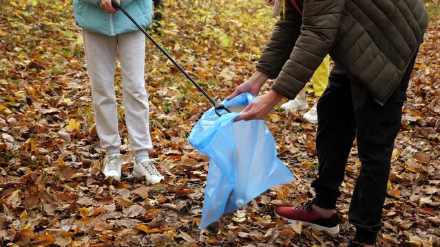 A group of activists collects garbage in a blue bag in the autumn forest, adults and children help clean up the forest.