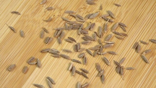 Dried cumin spice seeds falling down and rotate on wooden background. Dry seasoning cumin. Spices and herbs for cooking zira