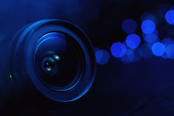 Camera lens in smoke and blue light close-up, lights out of focus on the background
