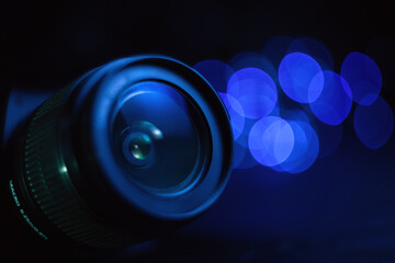 Camera lens in blue light close-up, lights out of focus on the background