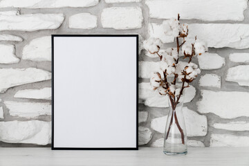 Mock up of black frame with white background. Cotton flowers and empty template on table. Shelf with interior decorations on stone wall. Copy space
