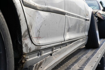 Close up view on crashed silver car, secured on aluminium trailer with damages in rear and side parts. Door sill frame and front and back doors are depressed.