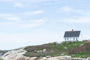 landscape view of old white house on the hill surrounded by flowers, grass and rocks near Peggy's cove Halifax Nova Scotia during beautiful sunny day
