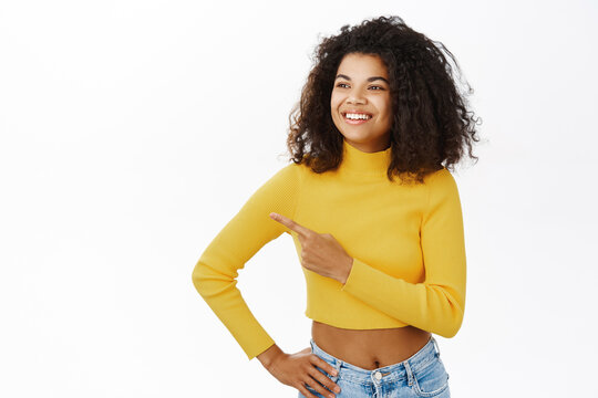 Smiling african american woman pointing finger left, showing advertisement, promo offer, standing against white background
