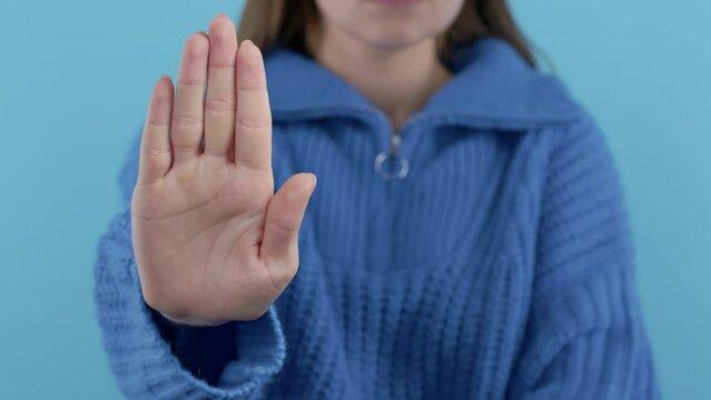 Serious woman showing rejecting gesture by stop finger sign. Enough signal. Lady on blue background.