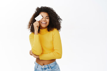 Beautiful Black girl shows her credit card, student id or discount in shop, looking happy, standing over white background - 554536090