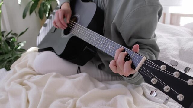 unrecognizable woman singing song and playing acoustic guitar in sunny cottage bedroom, hobby relaxing, girl pinches chords with her fingers