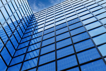 Low angle shot of the facade of a commercial building with blue windows under blue sky. Illustration of commercial and business district (CBD)