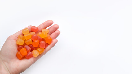 Group of red, orange and yellow multivitamin gummies in the hand isolated on white background