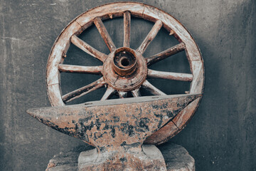 Wooden wheel of an old wagon on a wheathered , vintage colored wall and antique wrought iron tool in front. 	