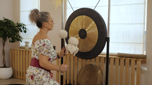Gong and gong mallets indoor. Woman taps the gong with soft hammers