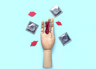 Wooden hand with lipstick, condoms and paper lips on blue background. Sex concept