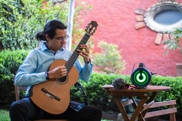 young hispanic man classical guitar player playing spanish classical music in a concert in a garden