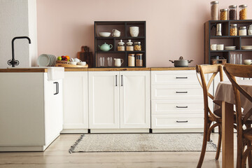 Counters with utensils and jars with food near light wall in kitchen