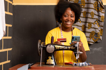 african tailor using her phone and credit card