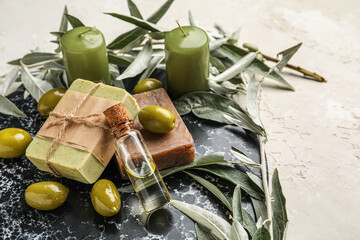 Board with soap bars, bottle of oil, green olives, branches and candles on white background