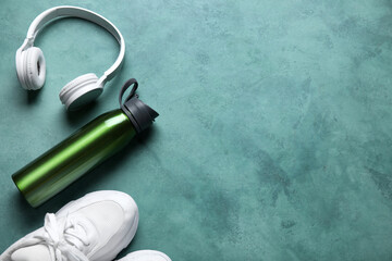 Obraz na płótnie Canvas Bottle of water, sneakers and headphones on green background