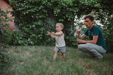 dad and son blowing soap bubbles in the backyard of the house in the summer