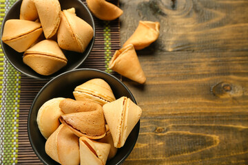 Bamboo mat with bowls of fortune cookies on wooden background, closeup