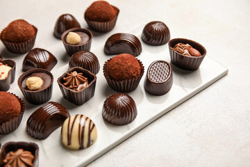 Board with chocolate candies on white background, closeup