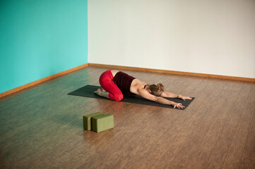 Woman in a studio practicing yoga wearing red yoga pants.