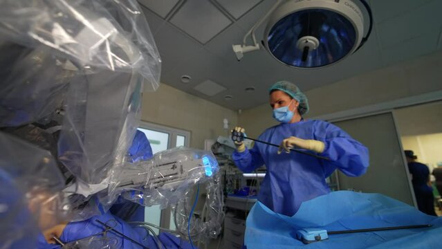 Female doctor takes the long nozzle from robotic arm from the table and attaches to machine. Robotic system performing the surgery. Low angle view.