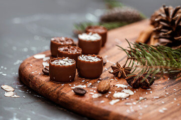Christmas table with wooden tray full of chocolates, almonds, coffee beans, anise stars with green pine branch and bokeh background