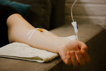 Woman's hand with catheter for dropper, butterfly needle used to draw blood from a vein or to deliver intravenous therapy to vein. Thin needle, flexible transparent tubing. Patient in nmedical clinic.