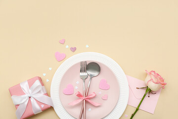 Table setting for Valentine's Day with pink rose, envelope and gift on beige background