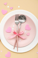 Table setting for Valentine's Day with bow and pink hearts on beige background