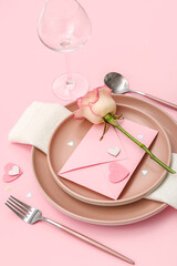 Table setting for Valentine's Day with envelope and rose on pink background