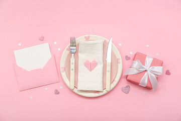 Table setting for Valentine's Day with envelope and gift on pink background