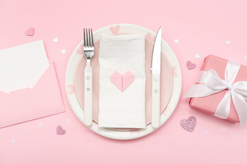 Table setting for Valentine's Day with envelope and gift on pink background