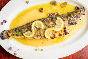 Grilled Fish. Branzino, whole grilled sea bream. Classic regional Greek  seafood favorite. Whole fish, grilled with skin in, served with lemon potatoes lemons Italian parsley and capers.