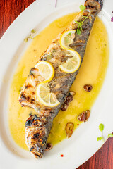 Grilled Fish. Branzino, whole grilled sea bream. Classic regional Greek  seafood favorite. Whole fish, grilled with skin in, served with lemon potatoes lemons Italian parsley and capers.
