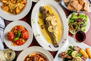 Grilled Fish. Italian Dinner table. Pasta, grilled sea bream. Classic regional Greek  seafood favorite. Whole fish, grilled with skin in, served with lemon potatoes lemons Italian parsley and capers.