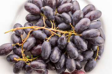 One bunch of juicy organic black grapes on a white ceramic platter, close-up, top view.