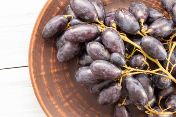 One bunch of juicy organic black grapes on a  ceramic platter on a wooden table, close-up, top view.